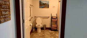Ein Badezimmer mit Toilette, Haltegriffen, einem Bild an der Wand und einem Handtuchregal.