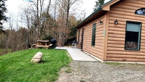 A log cabin with a porch, a picnic table, and a stone in the foreground. - Handicapped Accessible Log Cabin Rental near Smugglers' Notch Park, Vermont (Hyde Park)