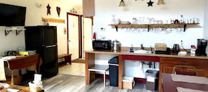 Une cuisine compacte équipée d’un réfrigérateur, d’un four à micro-ondes, d’un évier et d’une étagère où sont rangés la vaisselle.