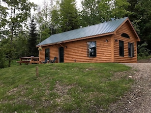 Une cabane en rondins avec un toit en métal, une table de pique-nique et une chaise à l’extérieur.
