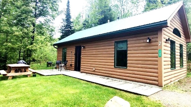 A log cabin with a green roof, two doors, and a small porch. - Handicapped Accessible Log Cabin Rental near Smugglers' Notch Park, Vermont (Hyde Park)