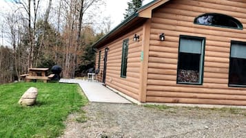 Une cabane en rondins avec une véranda, une table de pique-nique et un rocher au premier plan.
