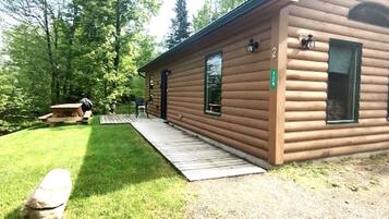 A log cabin with a wooden deck, a picnic table, and a small porch.