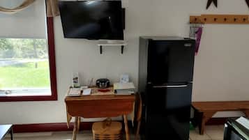 Uma pequena cozinha compacta com televisão, frigorífico e janela com vista para o verde.