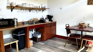 A compact kitchen with a microwave, sink, and wooden cabinets. There is a dining table with chairs and a sign on the wall. - Handicapped Accessible Log Cabin Rental near Smugglers' Notch Park, Vermont (Hyde Park)