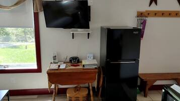 A small kitchenette with a TV, refrigerator, and a window with a view of greenery.