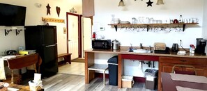 Una cocina compacta con refrigerador, microondas, pileta y una alacena con vajilla.