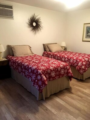 Una habitación con dos camas, cada una con una colcha floral roja, un respiradero en la pared y una decoración mural.
