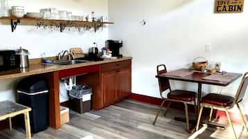 A compact kitchen with a microwave, sink, and wooden cabinets. There is a dining table with chairs and a sign on the wall.