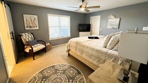 A bedroom with a bed, a chair, a desk, a ceiling fan, a TV, and artwork on the walls. - Luxury Lakeview Home with Expansive Two-Level Deck Near Beaver Lake | Rogers, Arkansas (Rogers)