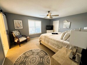 A bedroom with a bed, a chair, a desk, a ceiling fan, a TV, and artwork on the walls. - Luxury Lakeview Home with Expansive Two-Level Deck Near Beaver Lake | Rogers, Arkansas (Rogers)