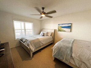 A bedroom with two beds, a ceiling fan, a window with blinds, and a painting on the wall. - Luxury Lakeview Home with Expansive Two-Level Deck Near Beaver Lake | Rogers, Arkansas (Rogers)
