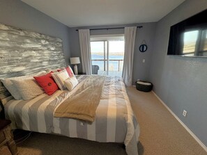A bedroom with a large bed, a view of the outdoors, and a television on the wall. - Luxury Lakeview Home with Expansive Two-Level Deck Near Beaver Lake | Rogers, Arkansas (Rogers)