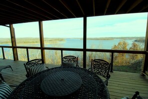 A covered outdoor area with a table and chairs, overlooking a body of water and trees. - Luxury Lakeview Home with Expansive Two-Level Deck Near Beaver Lake | Rogers, Arkansas (Rogers)