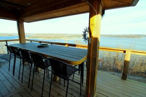 A wooden deck with a table and chairs, overlooking a body of water. - Luxury Lakeview Home with Expansive Two-Level Deck Near Beaver Lake | Rogers, Arkansas (Rogers)