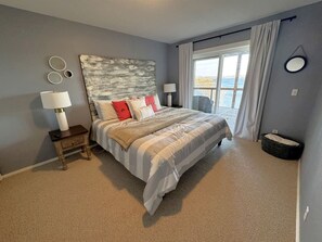 Een slaapkamer met een groot bed, twee nachtkastjes, een hoofdbord en uitzicht op het omliggende landschap door een raam.