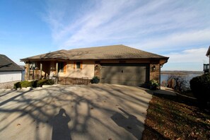 A single-story house with a garage, a covered porch, and a view of a body of water. - Luxury Lakeview Home with Expansive Two-Level Deck Near Beaver Lake | Rogers, Arkansas (Rogers)
