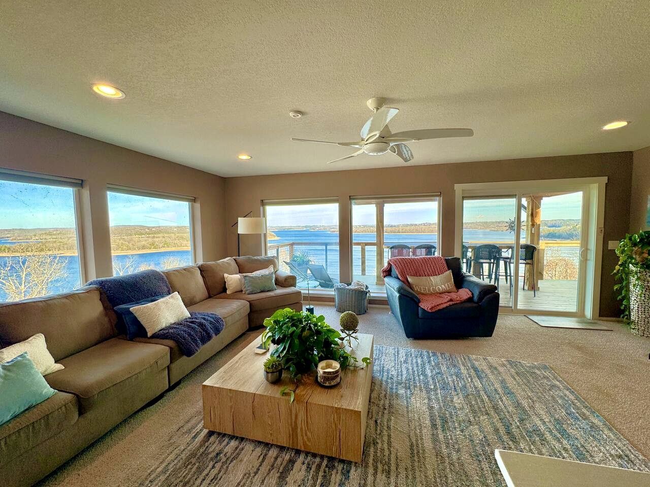 A spacious living room with a large sofa, a coffee table with plants, and a view of the outdoors through large windows.