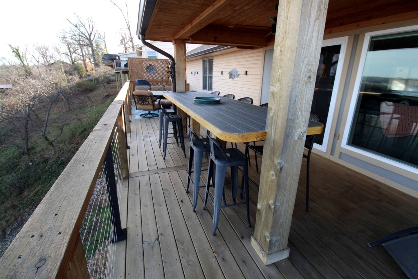 Une terrasse en bois avec une table et des chaises, un espace abrité et une vue sur une maison.