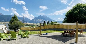 A patio area with green chairs, a picnic table, and a view of mountains. - Adventure-Ready A-Frame Cabins with Fire Pit & Cozy Mountain Setting in Emigrant, Montana (Emigrant)