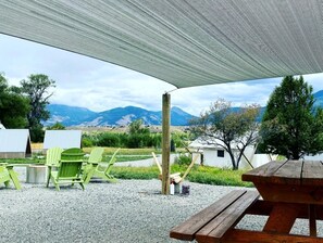 A covered outdoor seating area with a view of mountains, green chairs, and a wooden picnic table.