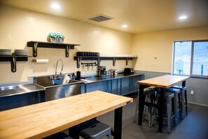 A kitchen with a sink, stove, and bar stools. - Adventure-Ready A-Frame Cabins with Fire Pit & Cozy Mountain Setting in Emigrant, Montana (Emigrant)