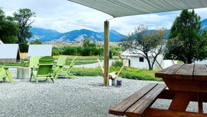 A covered outdoor seating area with a view of mountains, green chairs, and a wooden picnic table.