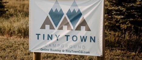 A sign for Tiny Town Campground with a mountain logo and online booking information.