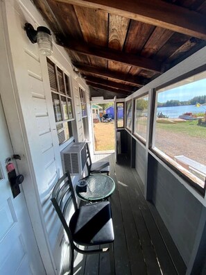 A covered porch with a table and chairs, a window with a view of a lake, and a door with a lock. - Lakefront Cottage Rental near Bear Brook State Park in Northwood, New Hampshire (Northwood)