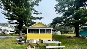A small yellow cabin with a porch, a grill, and a picnic table. - Lakefront Cottage Rental near Bear Brook State Park in Northwood, New Hampshire (Northwood)