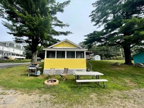 Eine kleine, gelbe Holzhütte mit Veranda, Grill und Picknicktisch.