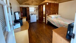 Ein kleines Zimmer mit einem Bett, einer Küchenzeile, einem Schreibtisch und einem Stuhl.