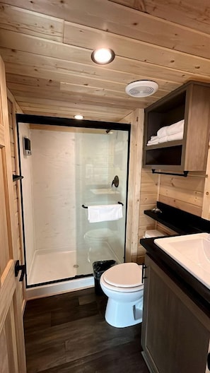 A wooden-paneled bathroom with a glass-enclosed shower, a white toilet, and a black countertop. - Serene Modern Retreat with Breathtaking Views & Stargazing in Williams, Arizona (Williams)