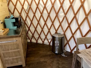 A room with a wooden floor, a metal trash can, a wooden table, and a white curtain with a diamond-patterned wooden frame.