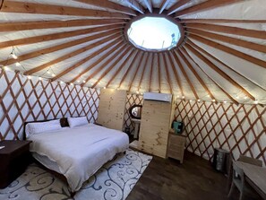 Una yurtas con una cama, un escritorio pequeño y un tragaluz circular.