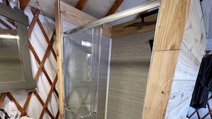 A shower enclosed by glass doors, a white sink, and wooden beams in a room under construction. - Texas Yurt for a Unique Glamping Holiday (Mineral Wells)