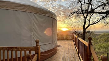 A wooden deck leading to a covered area with a view of a sunset and trees.