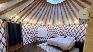 A yurt with a bed, a patterned rug, and a lattice wall.
