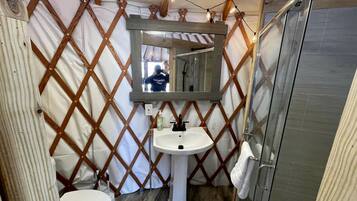 Een compacte badkamer met een houten lattenwand, een wastafel op voet, een spiegel en een douchecabine van glas.