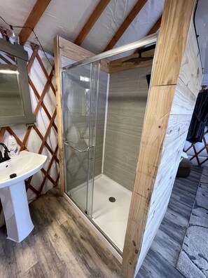 A shower enclosed by glass doors, a white sink, and wooden beams in a room under construction.