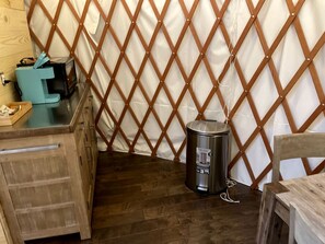 A room with a wooden floor, a metal trash can, a wooden table, and a white curtain with a diamond-patterned wooden frame.