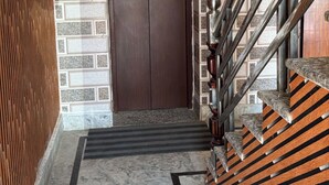 Ein Flur mit Marmorboden, einer Holzverkleidung, einer braunen Tür und einer Treppe mit Metallgeländer.