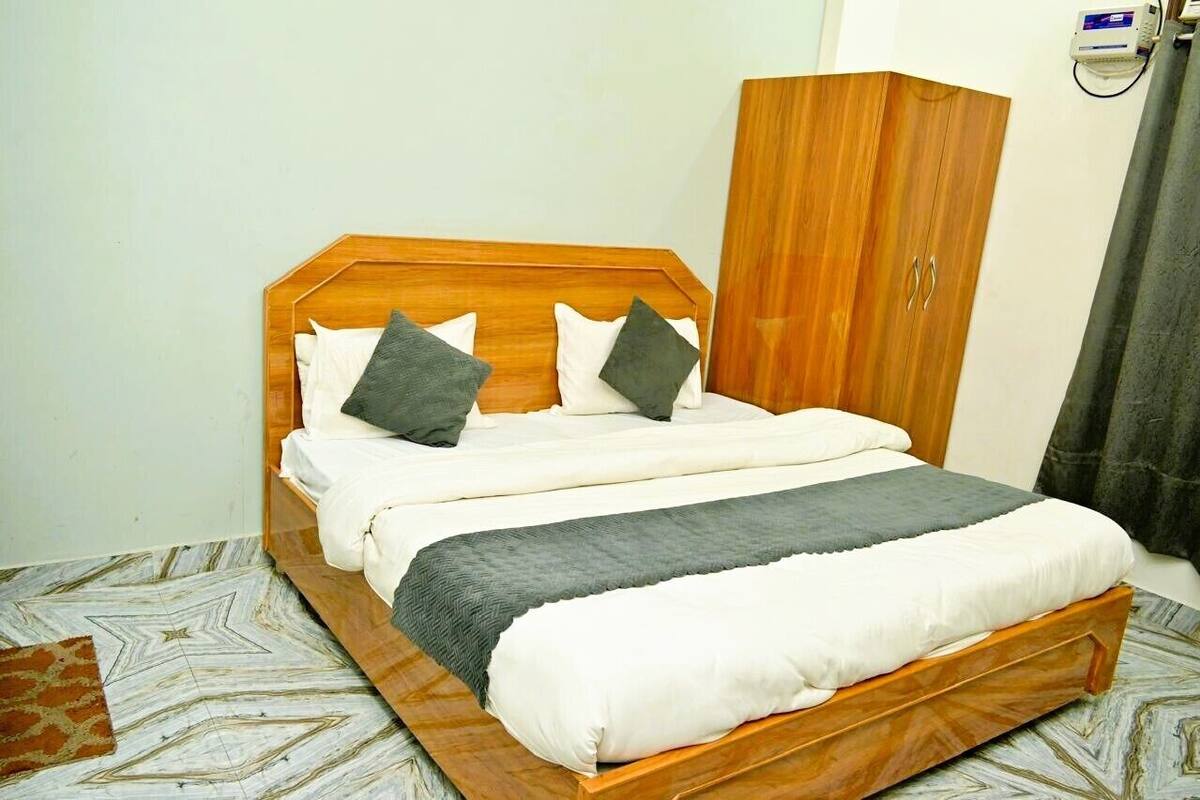 Una cama con cabecera de madera, manta gris y dos almohadas.