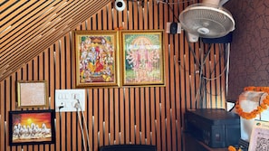 Une pièce aux murs recouverts de lambris en bois, avec un ventilateur de plafond, une imprimante et des œuvres d’art religieux encadrées.