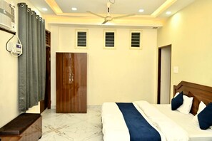 A bedroom with a bed, a ceiling fan, a wardrobe, and a window with blinds. - Hotel Raghunath Residency (Kanpur)