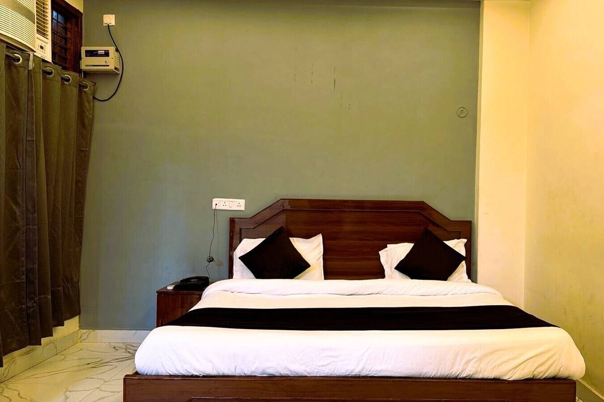 Una cama bien hecha con cabecera de madera, una mesita de noche con lámpara y un aire acondicionado instalado en la pared.