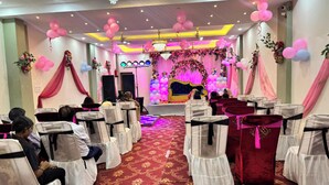 Ein Bankettsaal mit Reihen von Stühlen, einer Bühne mit Blumendekorationen und einer Kristallleuchter.