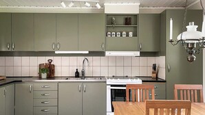 A kitchen with green cabinets, a white stove, and a wooden dining table. - 4 Star Holiday Home in Vato (Vätö)