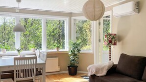 A room with a dining table, chairs, a sofa, a small table with a bowl, and large windows with a view of greenery. - 4 Star Holiday Home in Vato (Vätö)