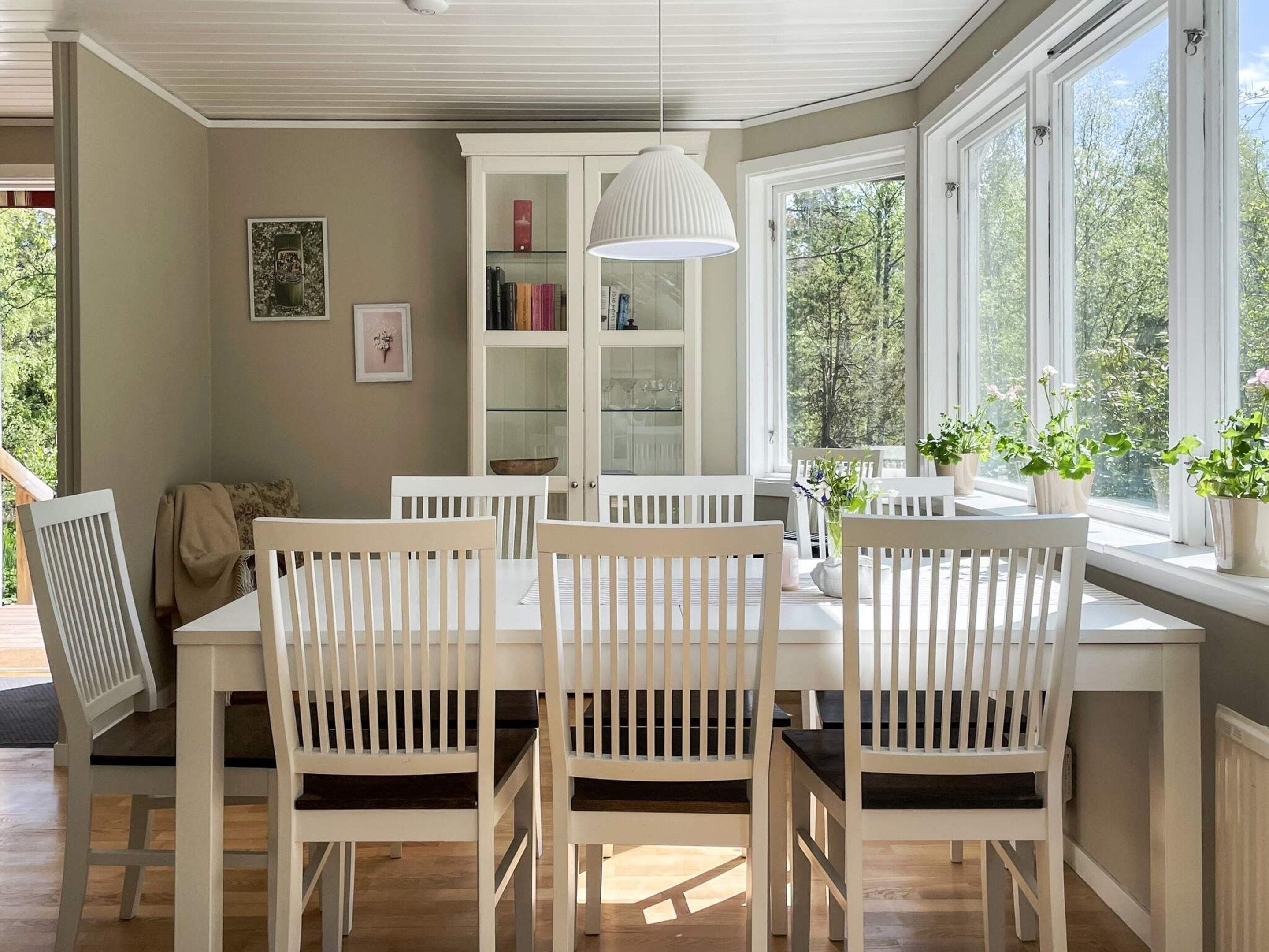 A dining area with a white table and chairs, a white pendant light, and a bookshelf.